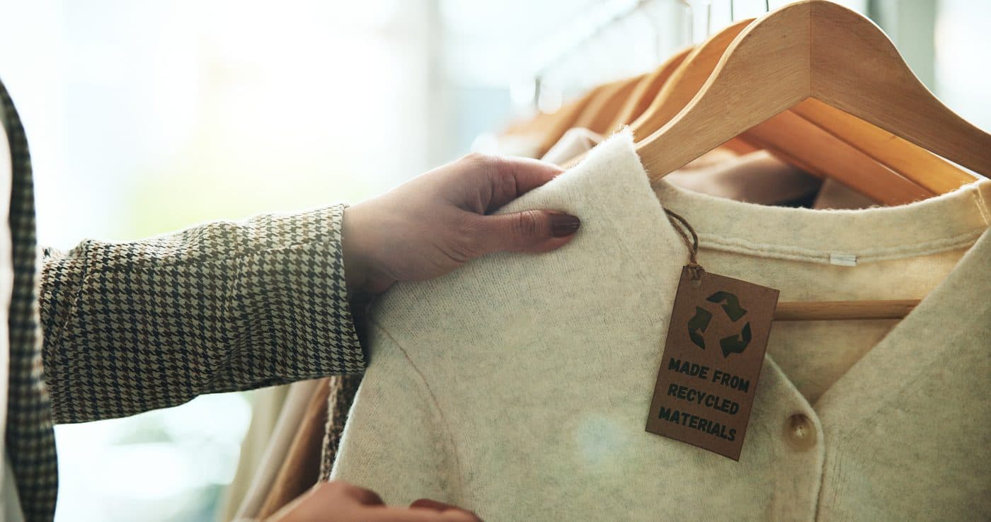 Eine Hand hält ein Etikett mit der Aufschrift „aus recycelten Materialien“